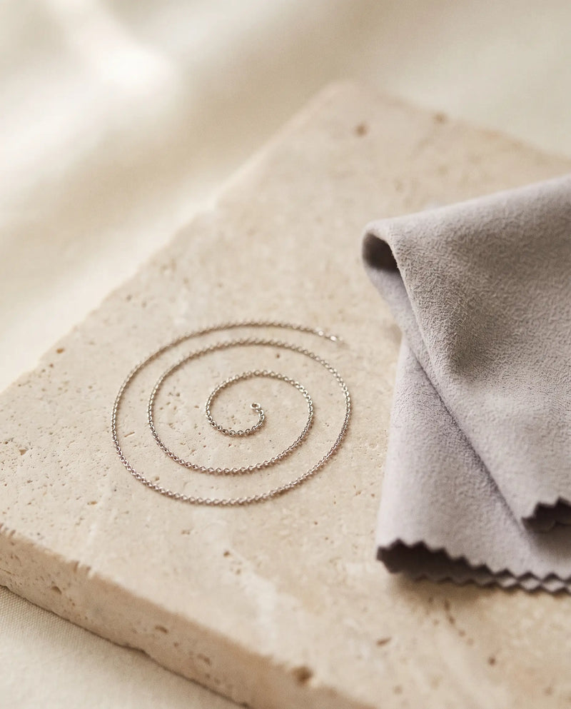 A fine silver-tone chain coiled beside a soft polishing cloth
