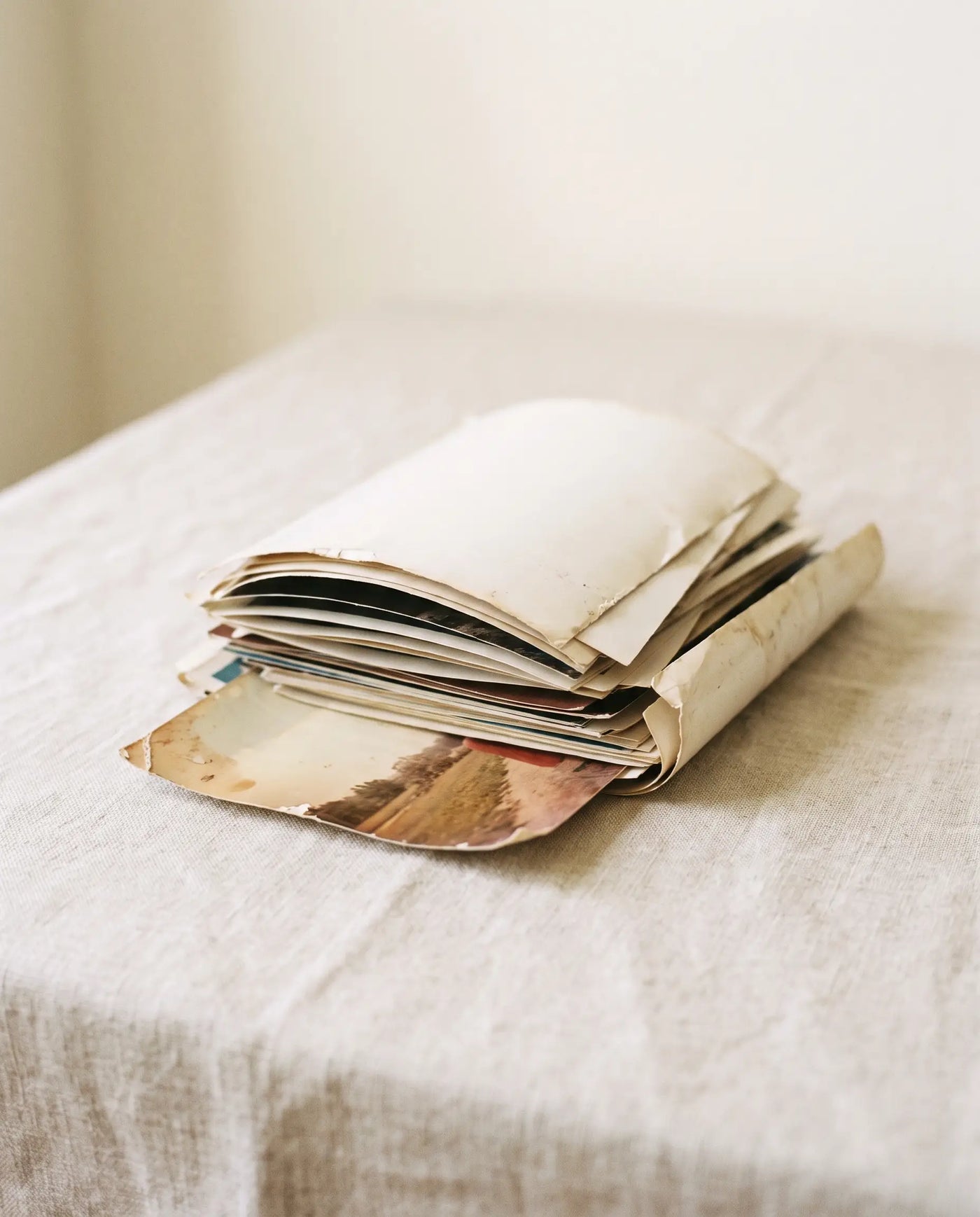 A loose stack of old printed photographs on a linen surface