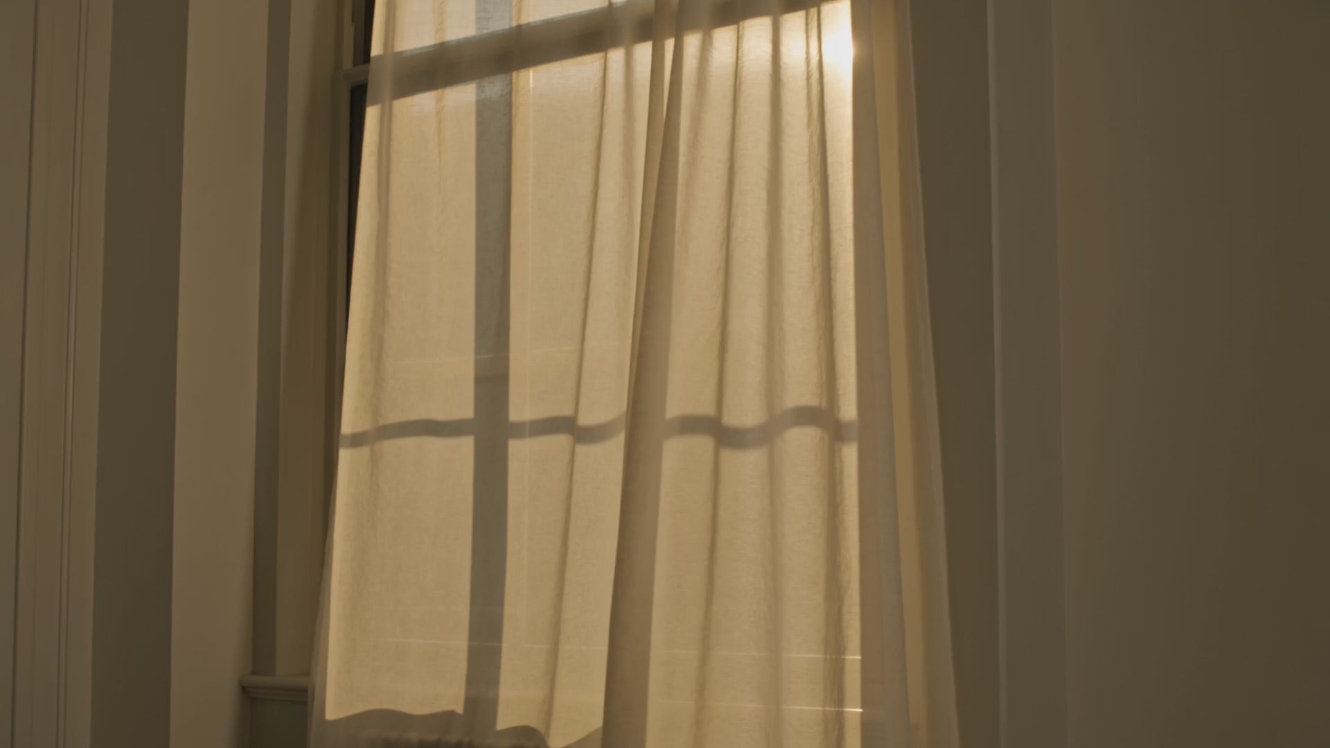 Load video: A sheer cream curtain drifting in warm afternoon window light