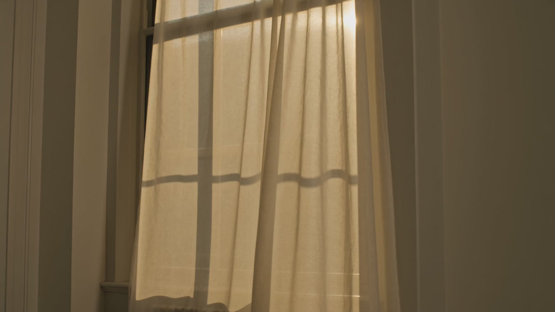 A sheer cream curtain drifting in warm afternoon window light